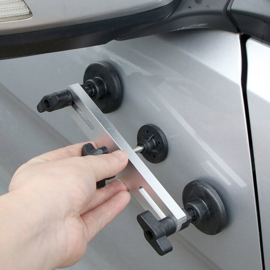 Dent pulling bridge tool on a silver SUV fender