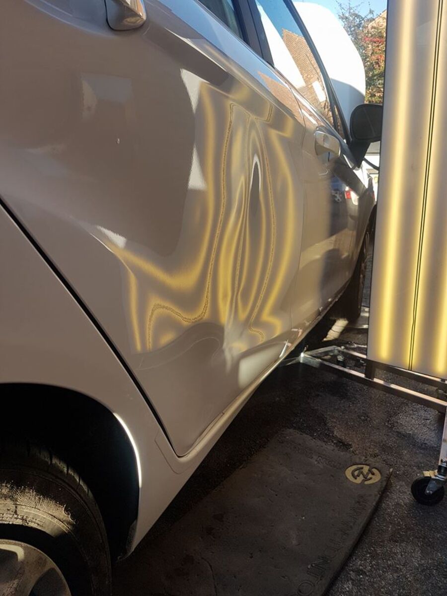Hail dents on a car door shown under PDR light